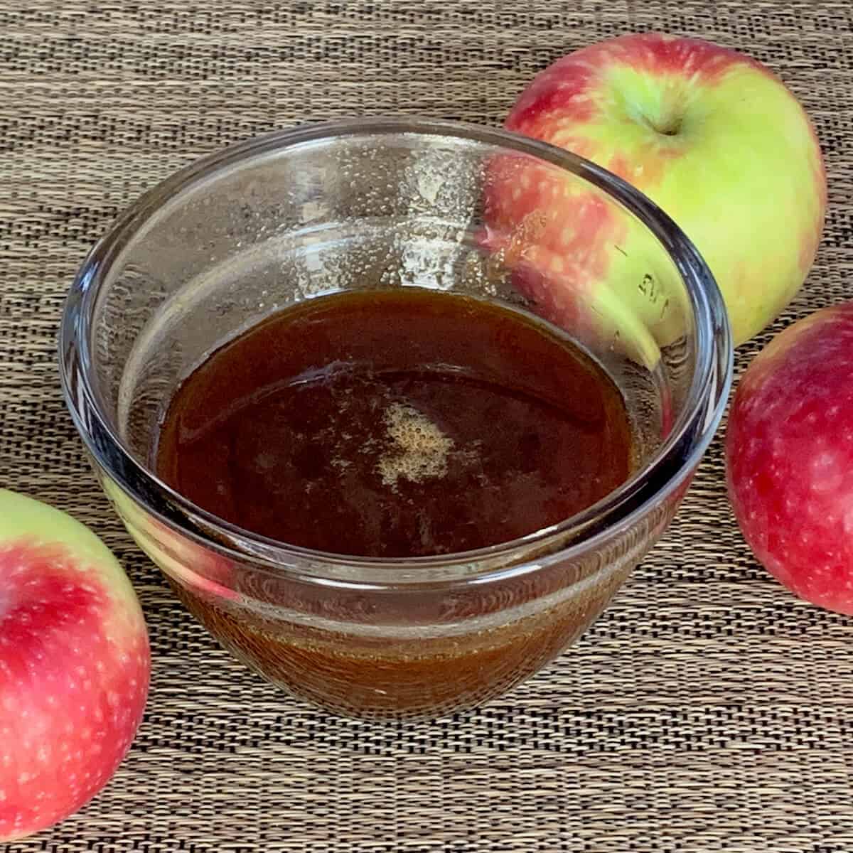 Boiled apple cider in a glass bowl with apples.