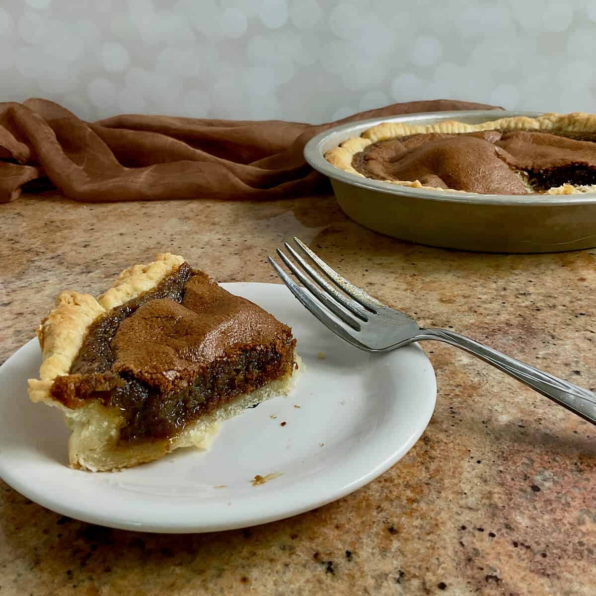 Partially eaten slice of Brown Sugar Pie on a white plate and fork with the sliced pie in the pie pan in background.