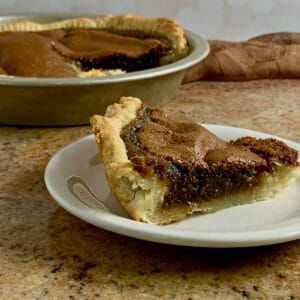 Slice of Brown Sugar Pie on a white plate with the sliced pie in the pie pan in background.