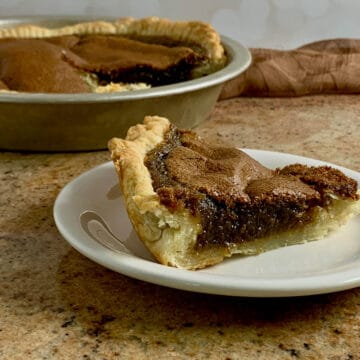 Slice of Brown Sugar Pie on a white plate with the sliced pie in the pie pan in background.