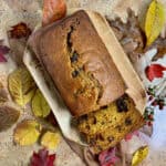 Sliced Pumpkin Bread on a wood tray surrounded by Fall leaves on a brown scarf.