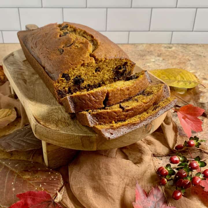 Sliced Pumpkin Bread on a wood tray surrounded by Fall leaves on a brown scarf.