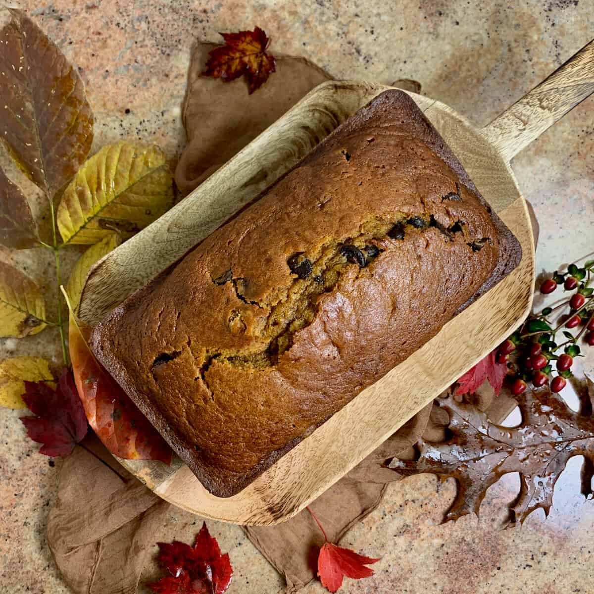 Whole Pumpkin Bread on a wood tray surrounded by Fall leaves on a brown scarf from overhead.