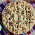 Lattice topped apple pie on a purple striped towel with cut apples from overhead Pinterest banner.