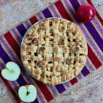 Lattice topped apple pie on a purple striped towel with cut apples from overhead.