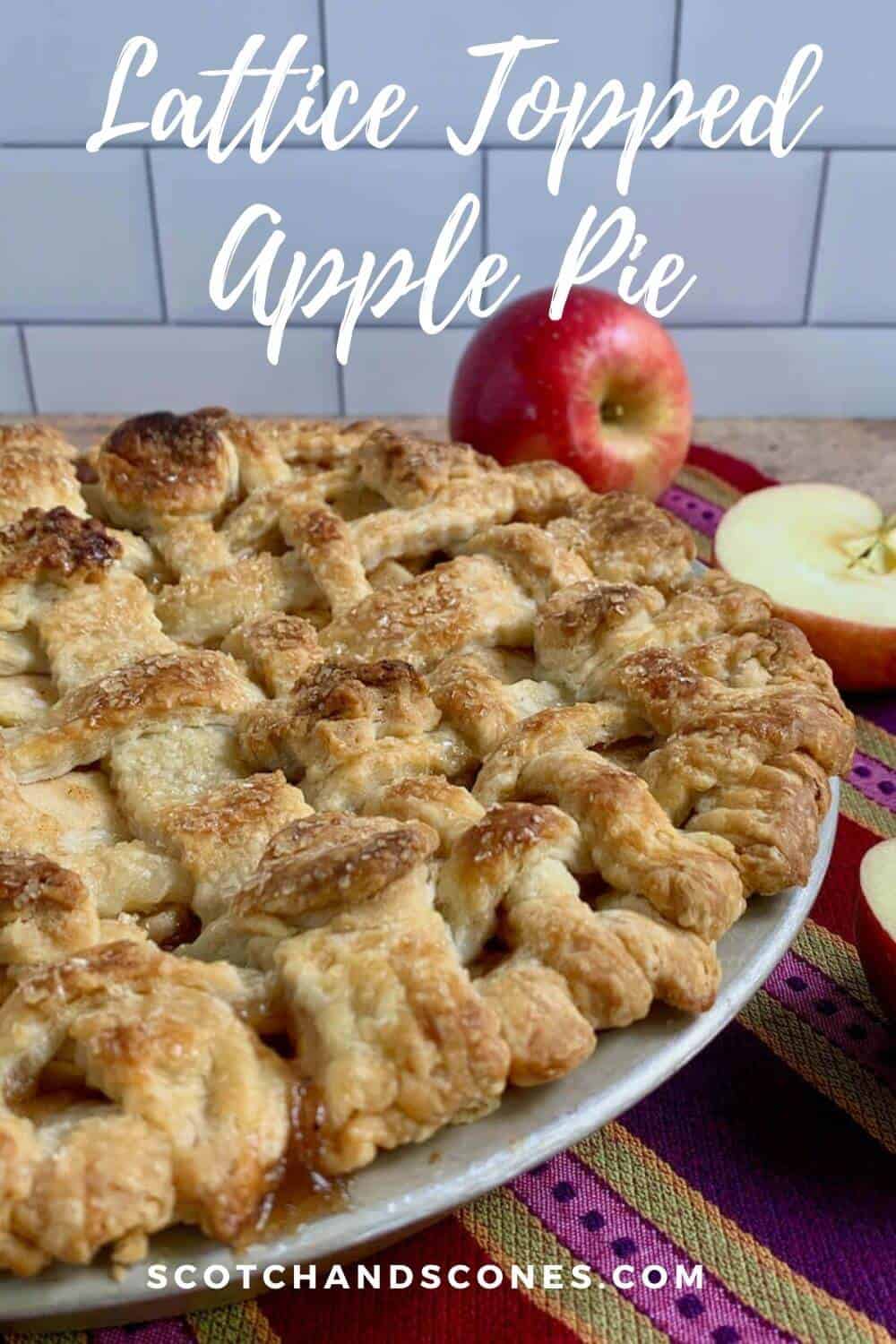Lattice topped apple pie on a purple striped towel with cut apples Pinterest banner.