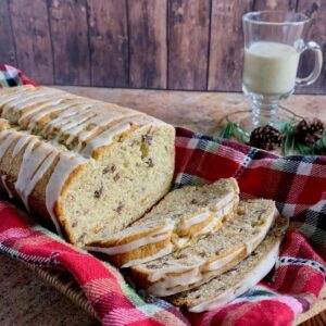 Sliced eggnog bread on a plaid towel in a basket with mug of eggnog behind.