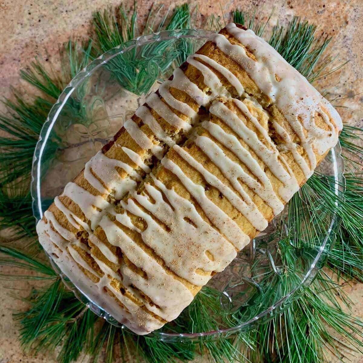 Whole eggnog bread on a glass cake stand atop pine needles from overhead.