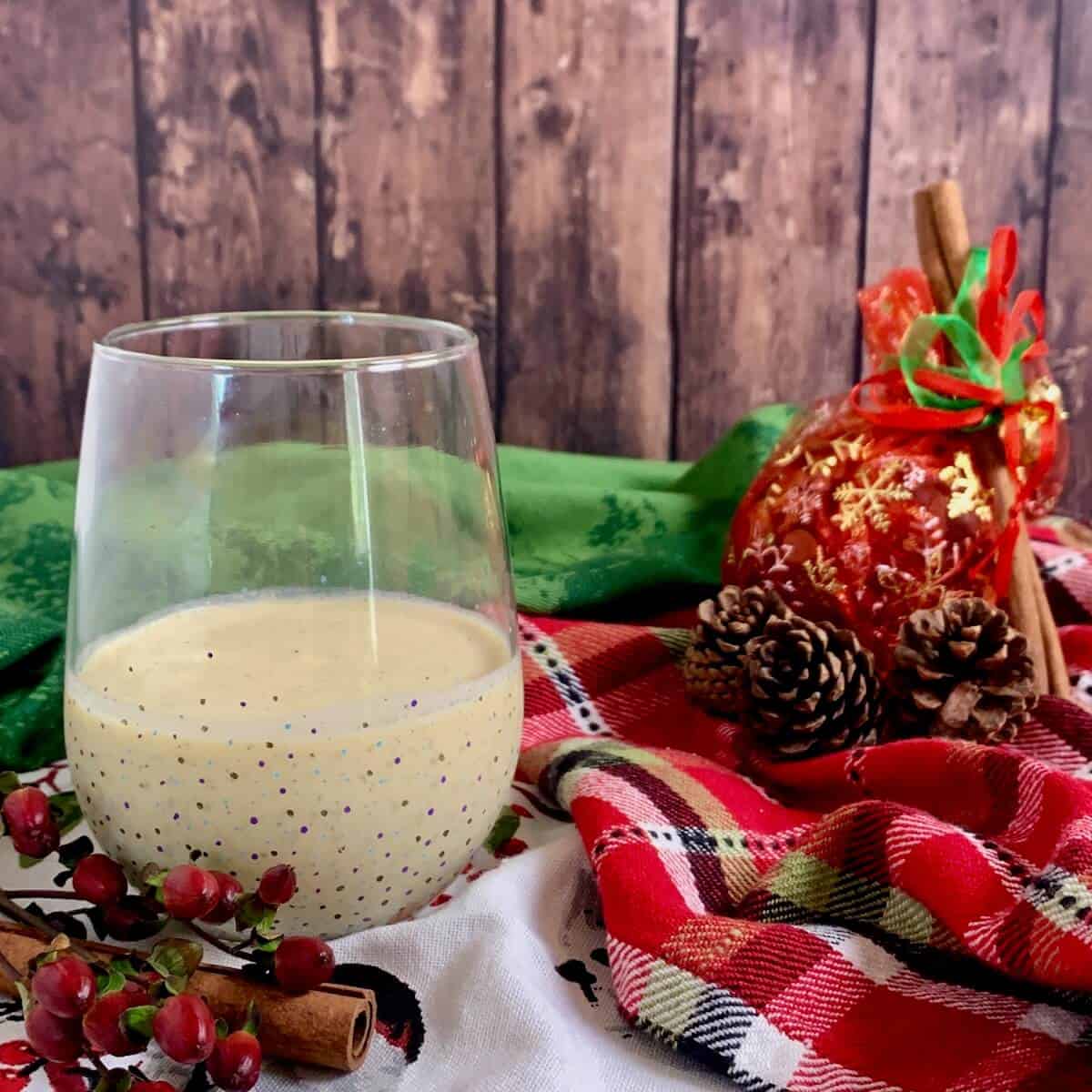 Glass of eggnog with pinecones & Christmas ornament on top of festive towels.