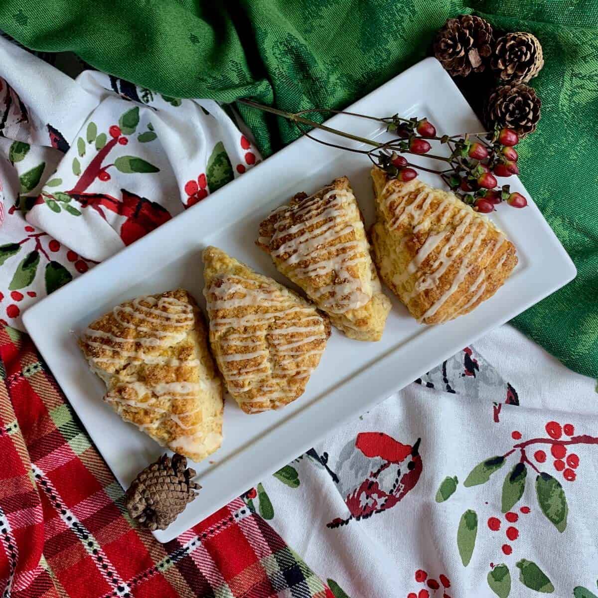 Four Eggnog Scones alongside red berries and mini pinecones on a white plate.