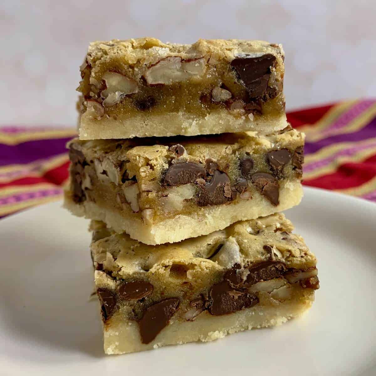 Three pecan bars stacked on top of each other on a white plate with a red striped towel behind.