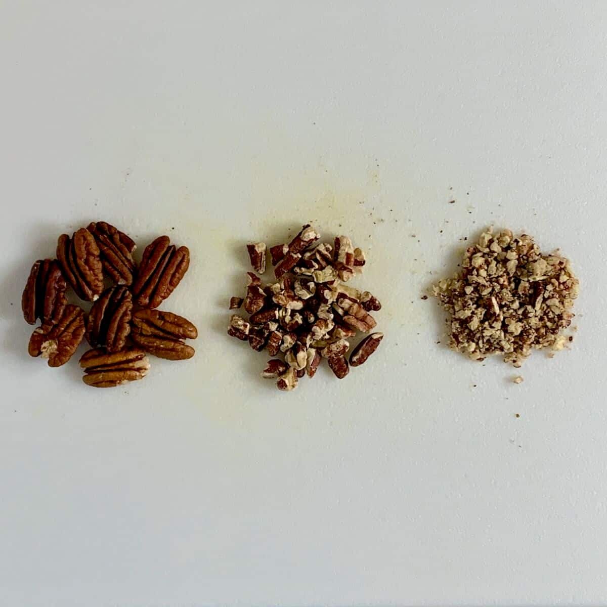 Comparison of whole pecans, coarsely chopped, and finely chopped next to each other.