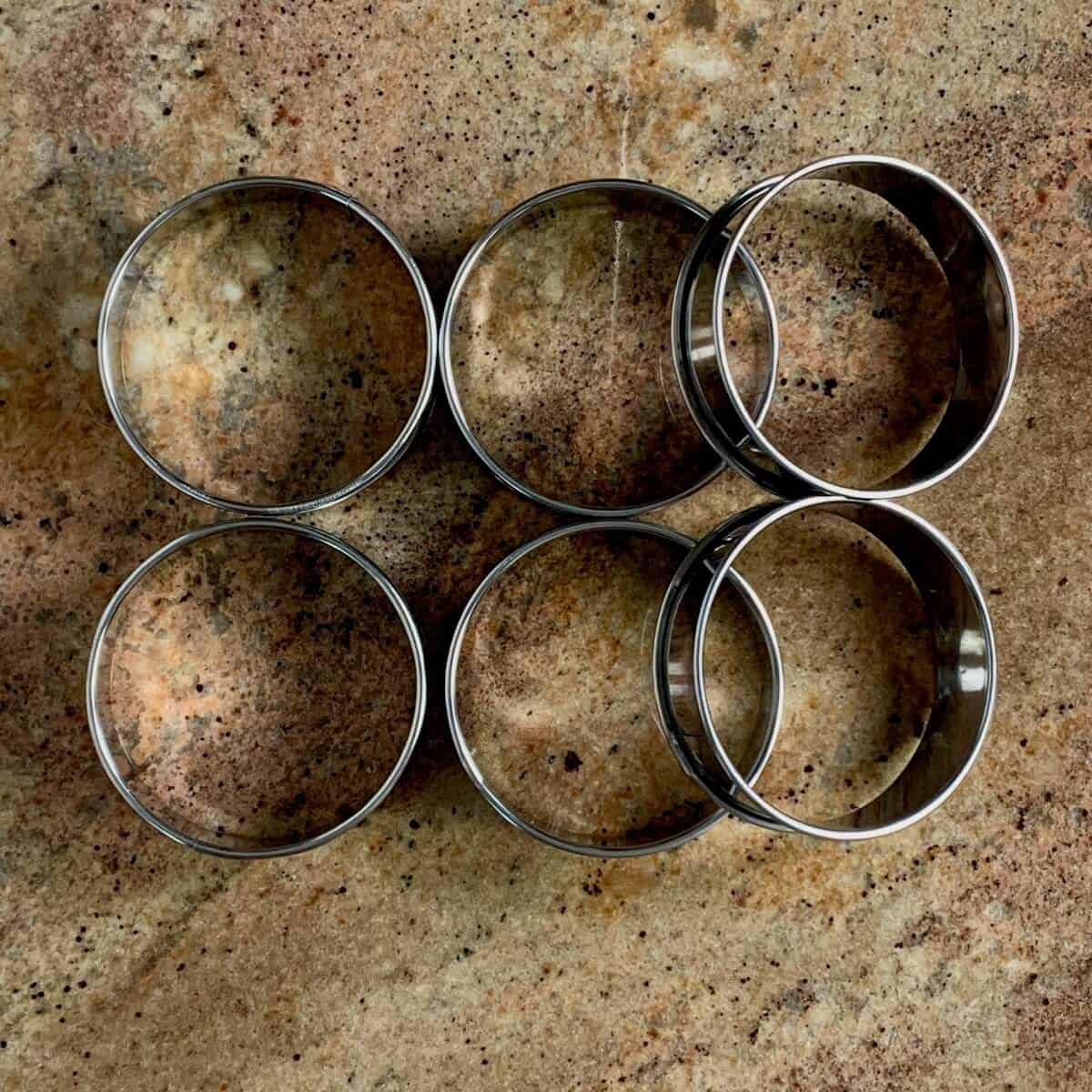 Six English muffin rings on a counter from overhead.