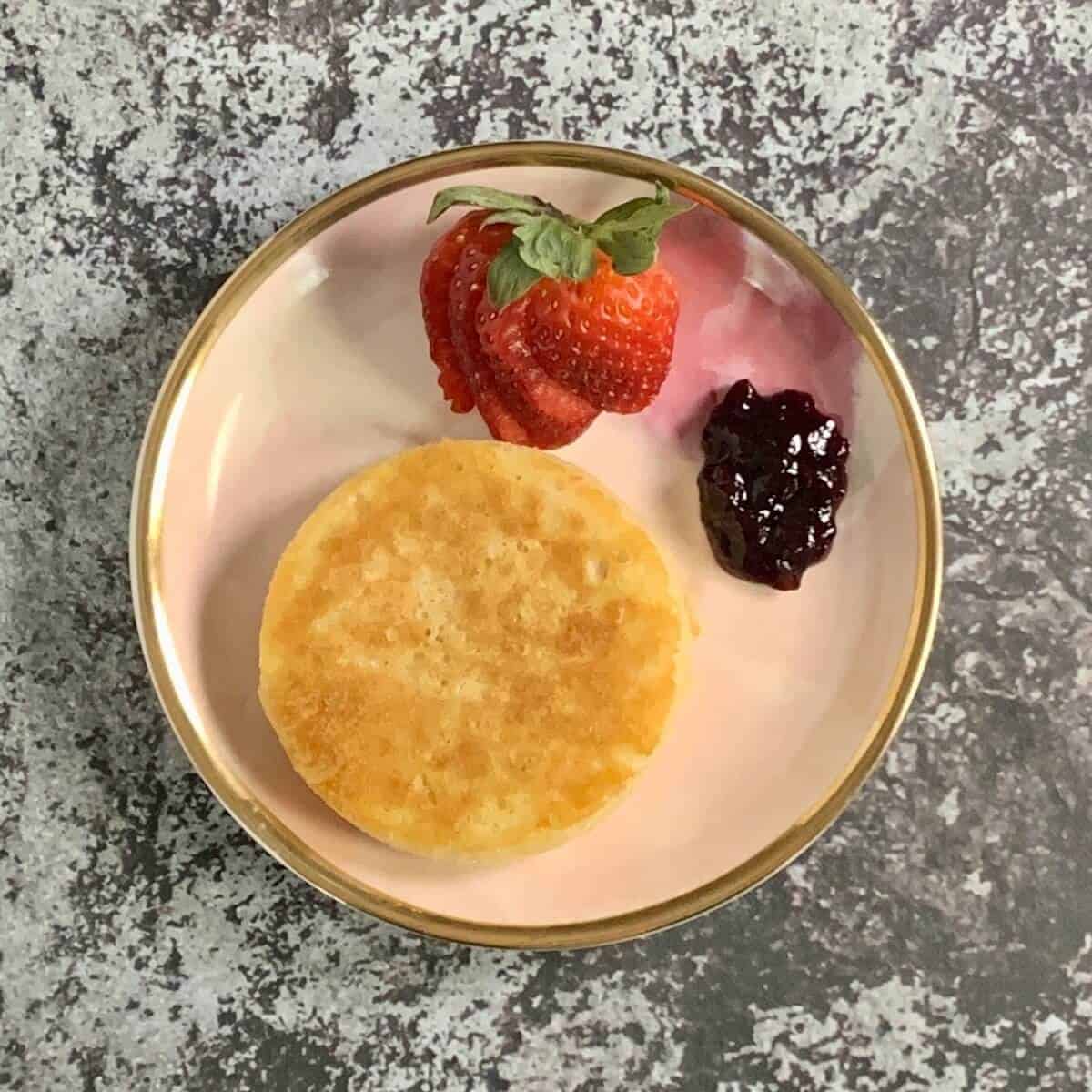 Crumpet on a plate with a sliced strawberry and jam from overhead.