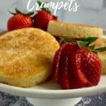 Three crumpets stacked on a white cakestand surrounded by strawberries Pinterest banner.