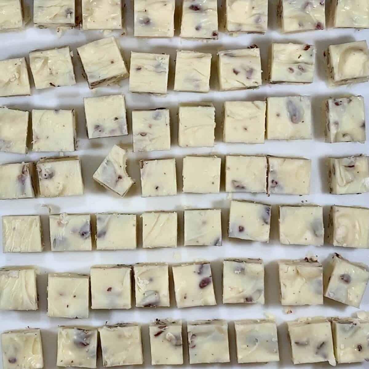 White chocolate pecan fudge cut into squares on a cutting board.