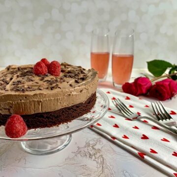 Chocolate Mousse Cake next to a heart-spotted towel with 2 forks, champagne glasses, and roses.