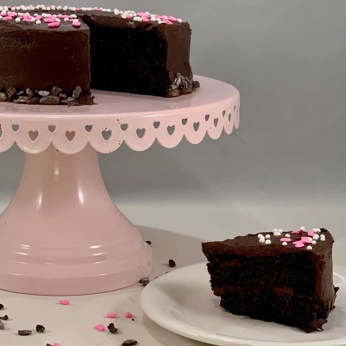 Port wine dark chocolate cake on a pink cake stand with slice on a white plate.