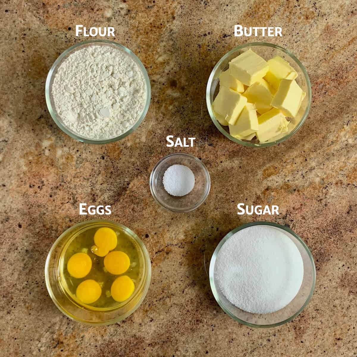 Pound cake ingredients flour, butter, eggs, sugar, and salt in glass bowls.