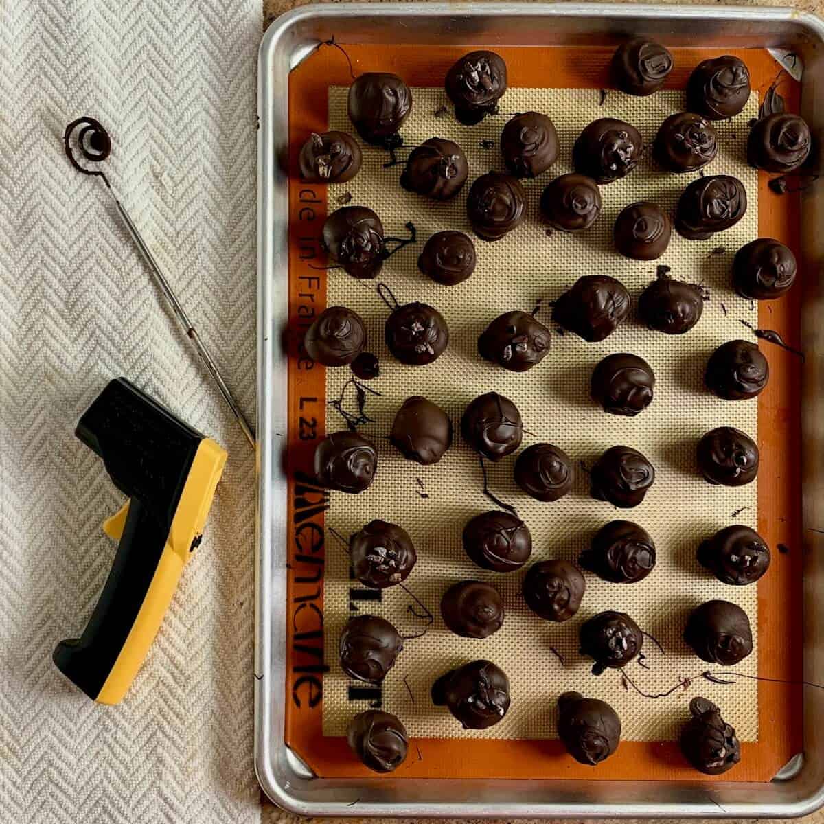 Chocolate cake truffles on a baking pan with infrared temperature gun & dipping tool from overhead.