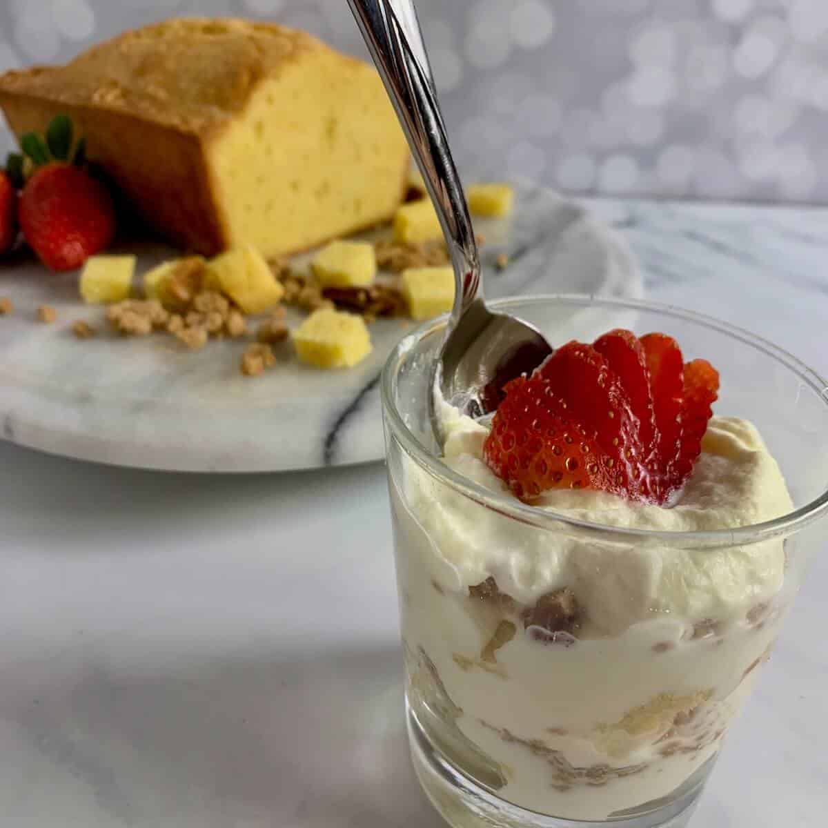 A serving of Orange Cinnamon Trifle with a spoon and a pound cake and another serving in background.