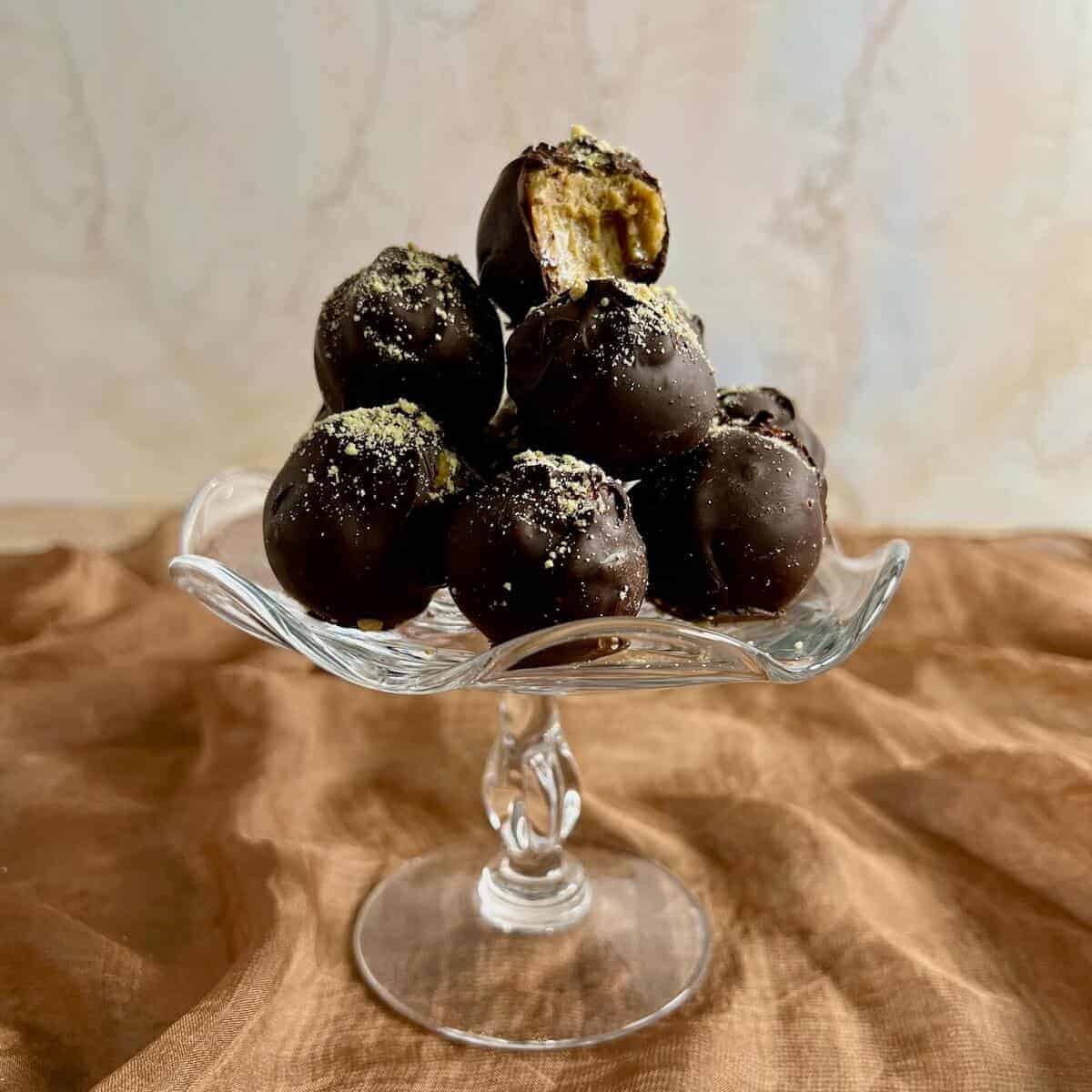 Tiramisu truffles stacked on a glass stand with top one bitten..