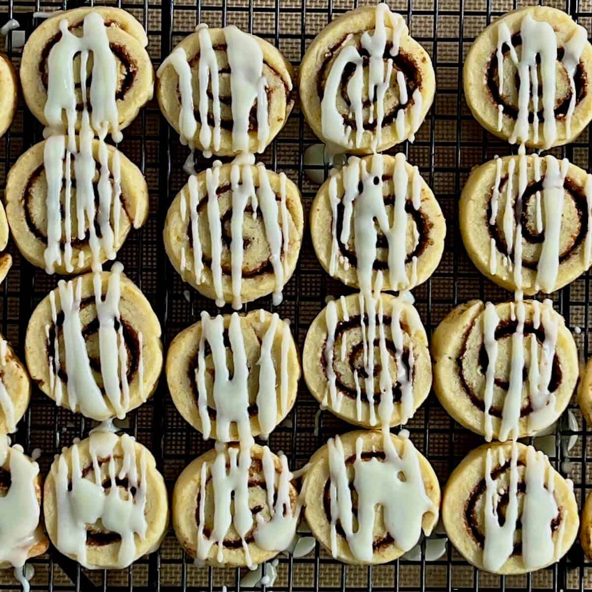 Glazed cinnamon roll cookies drying in rows on a rack from overhead.