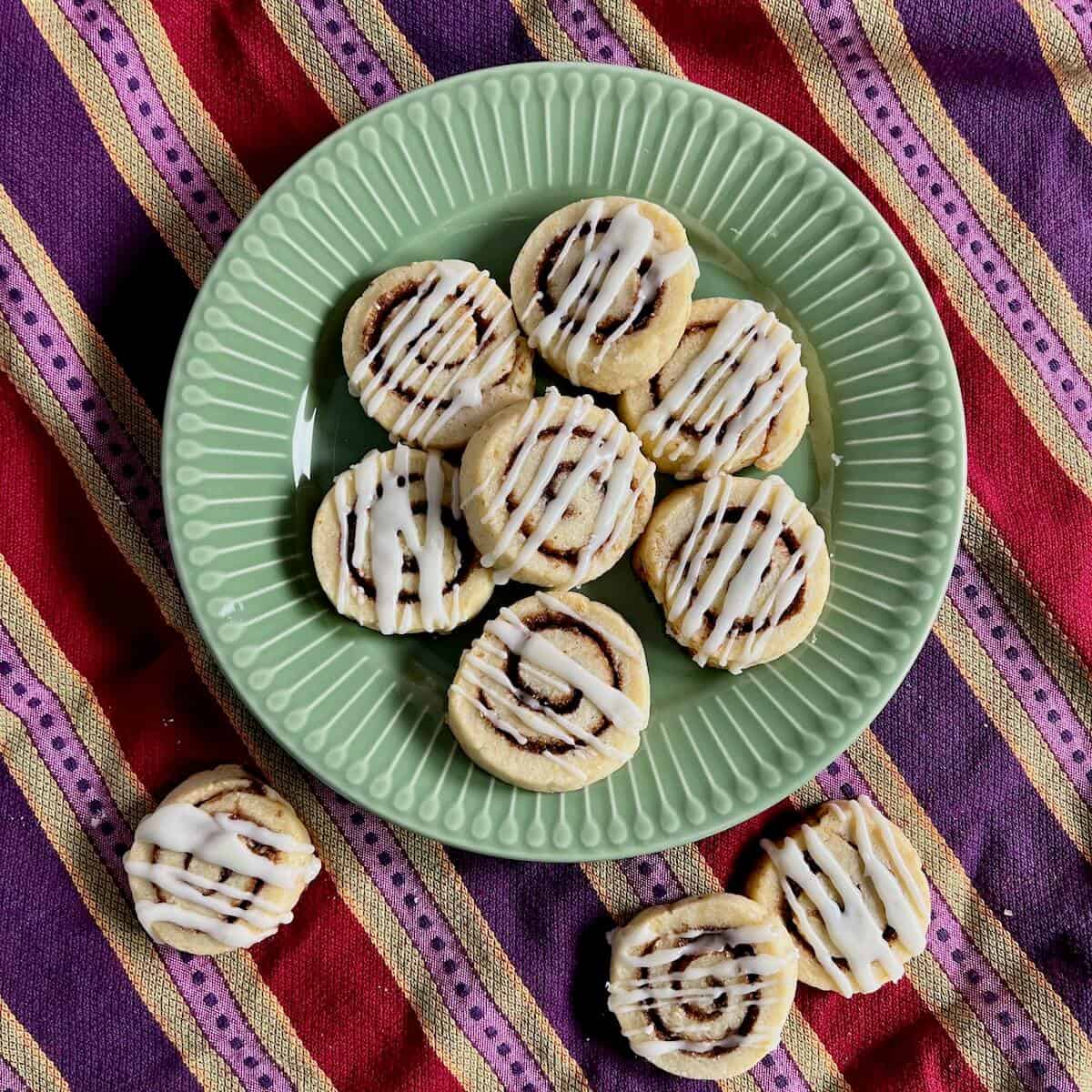 Three cinnamon roll cookies on a striped towel beside more on a green plate from overhead.