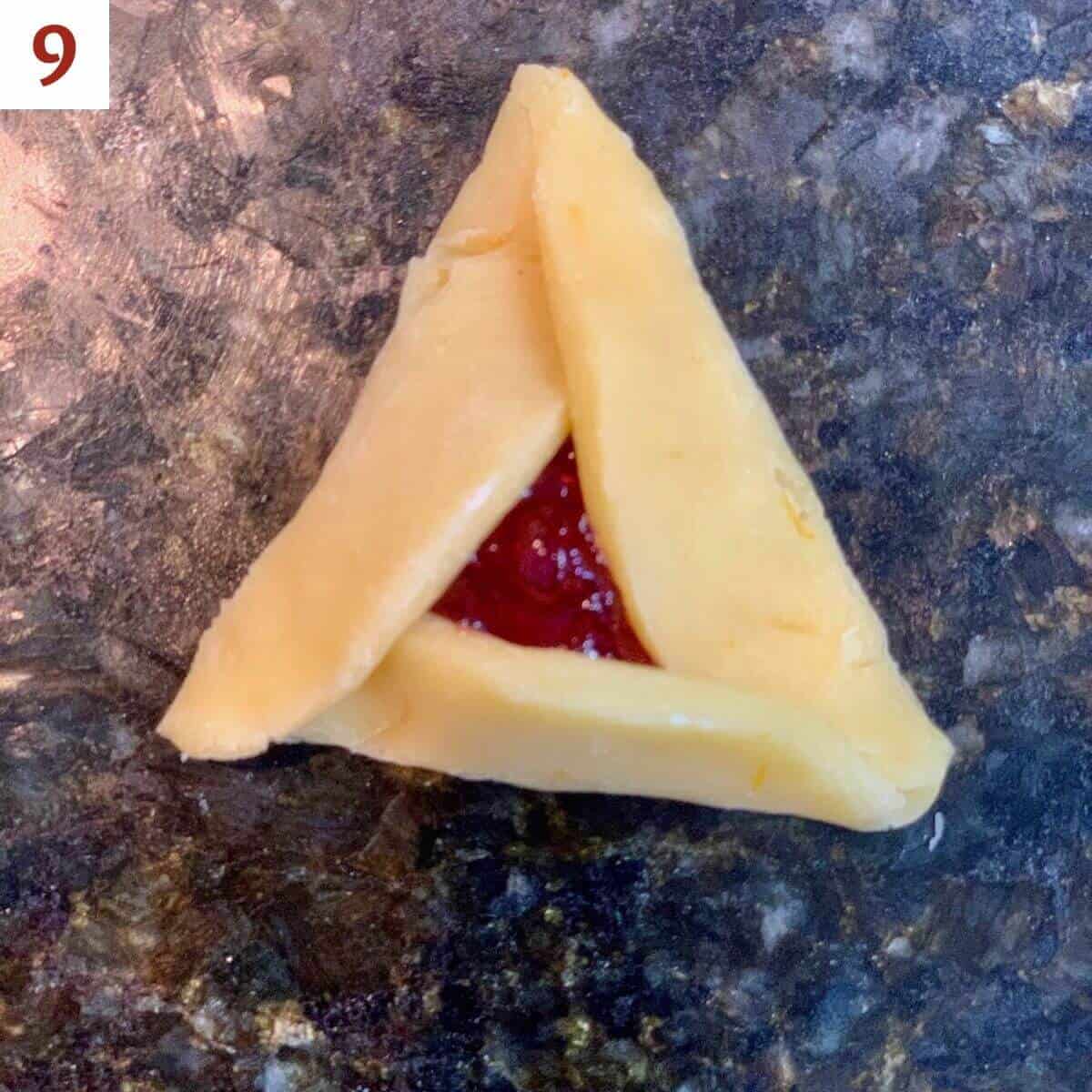 Fully shaped unbaked hamantaschen cookie on a black marble counter.