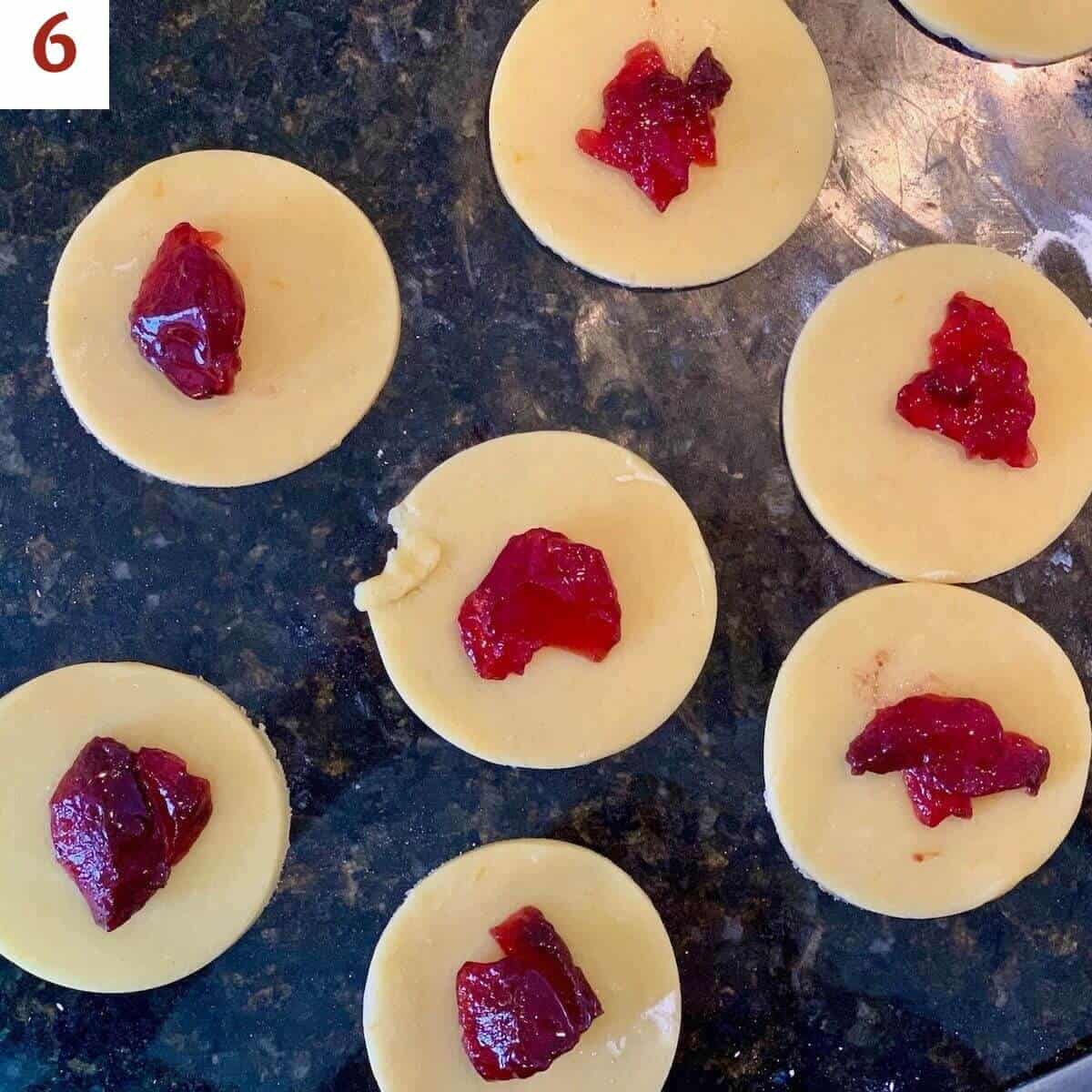 Jelly atop circles of sugar cookie dough on a black marble counter.