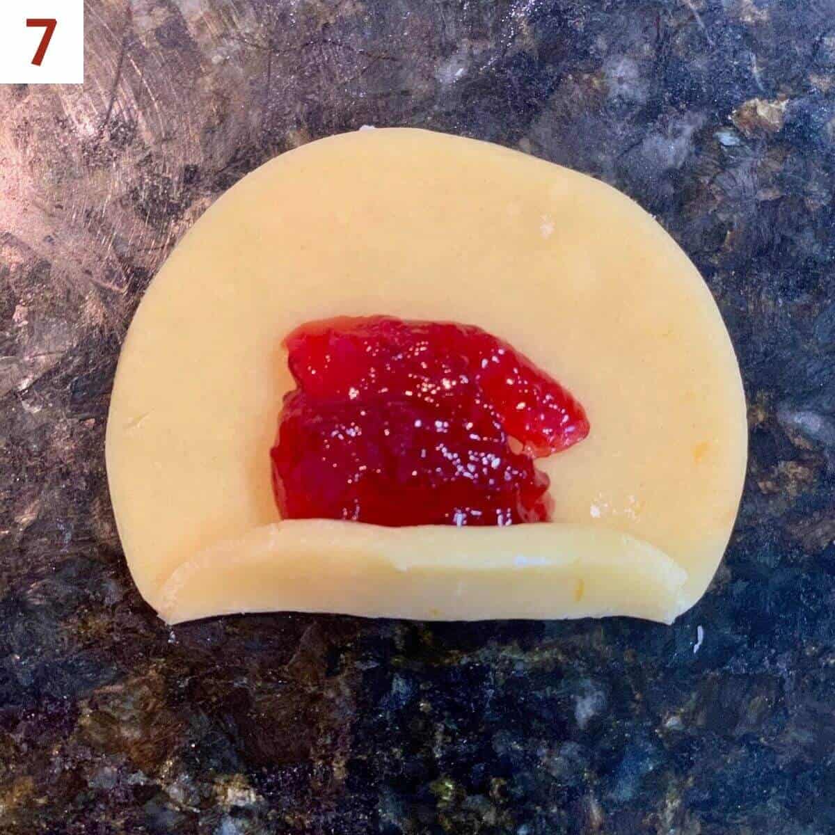 Folding up one side of a jam-filled dough circle on a black marble counter.