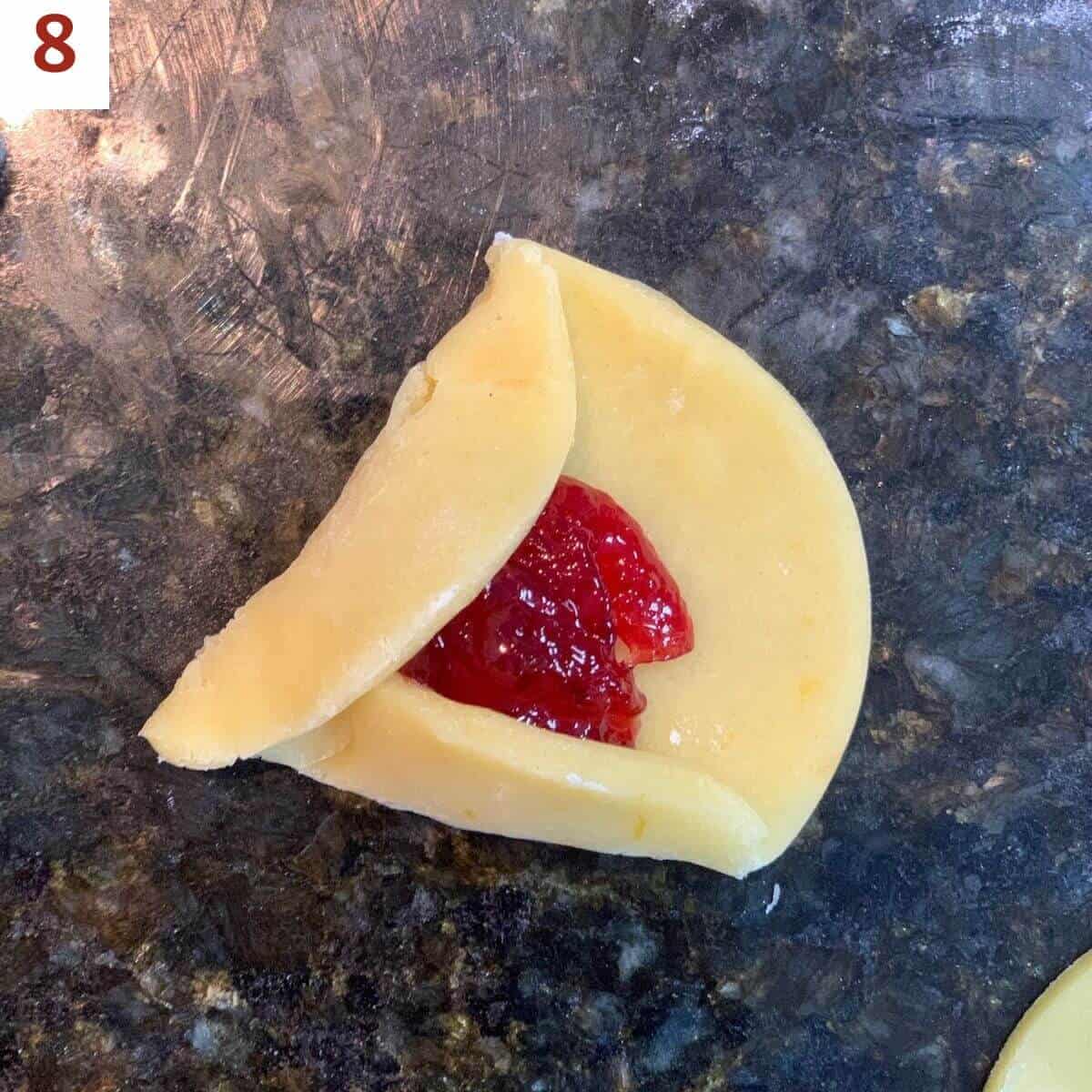 Folding up two sides of a jam-filled dough circle on a black marble counter.