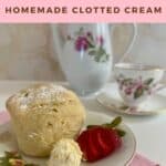 Clotted cream alongside a scone & cut strawberry on a flowered plate with teapot & teacup behind Pinterest banner.