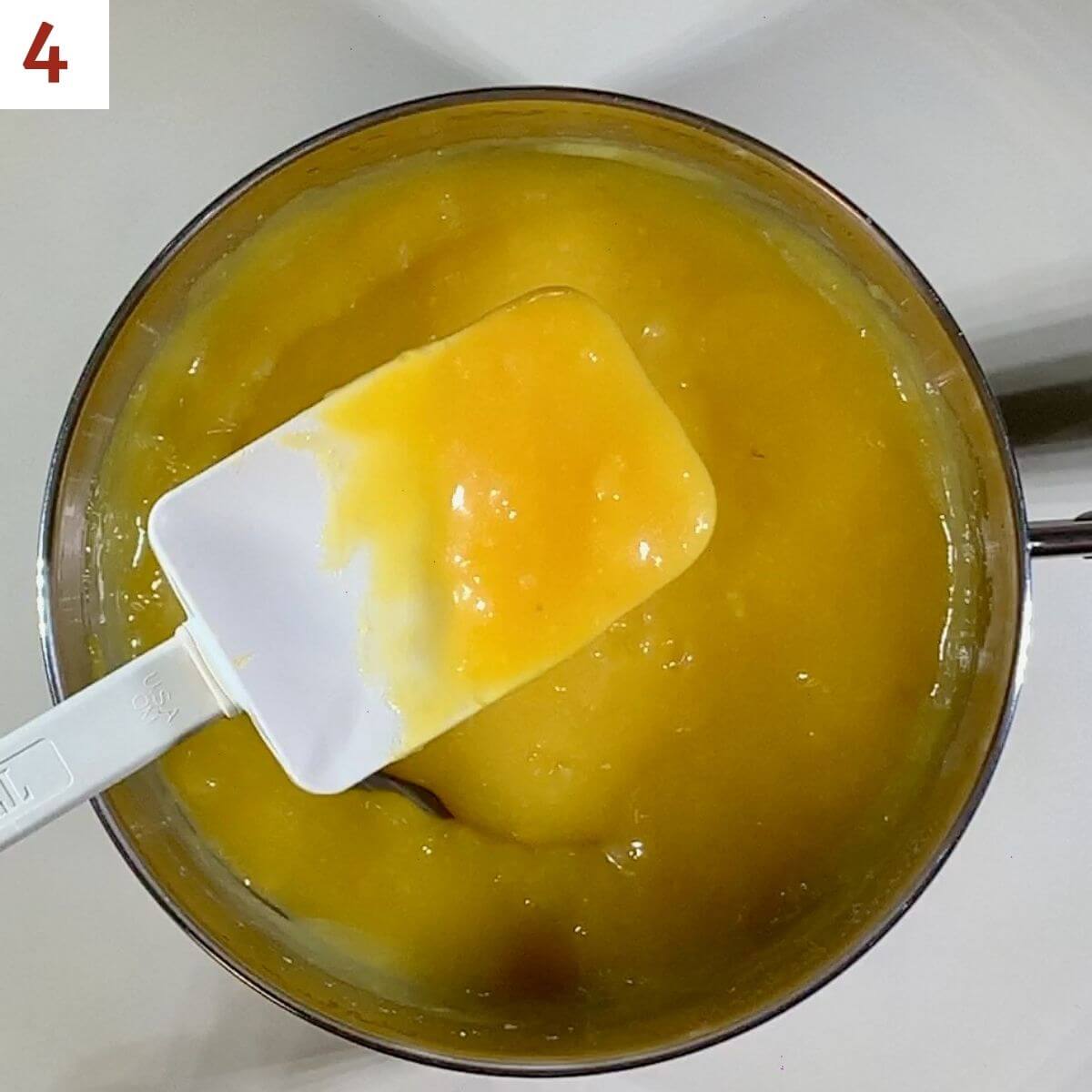 Cooled thickened lemon curd on a spatula above its pot.