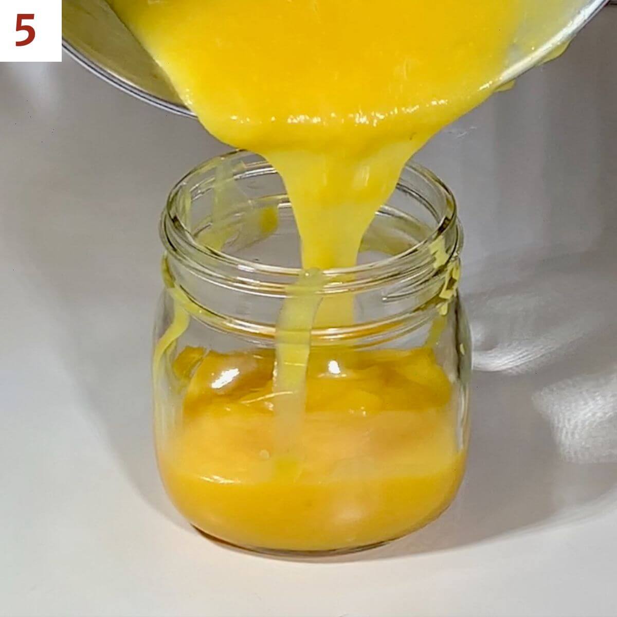 Finished lemon curd being poured into a glass jar.
