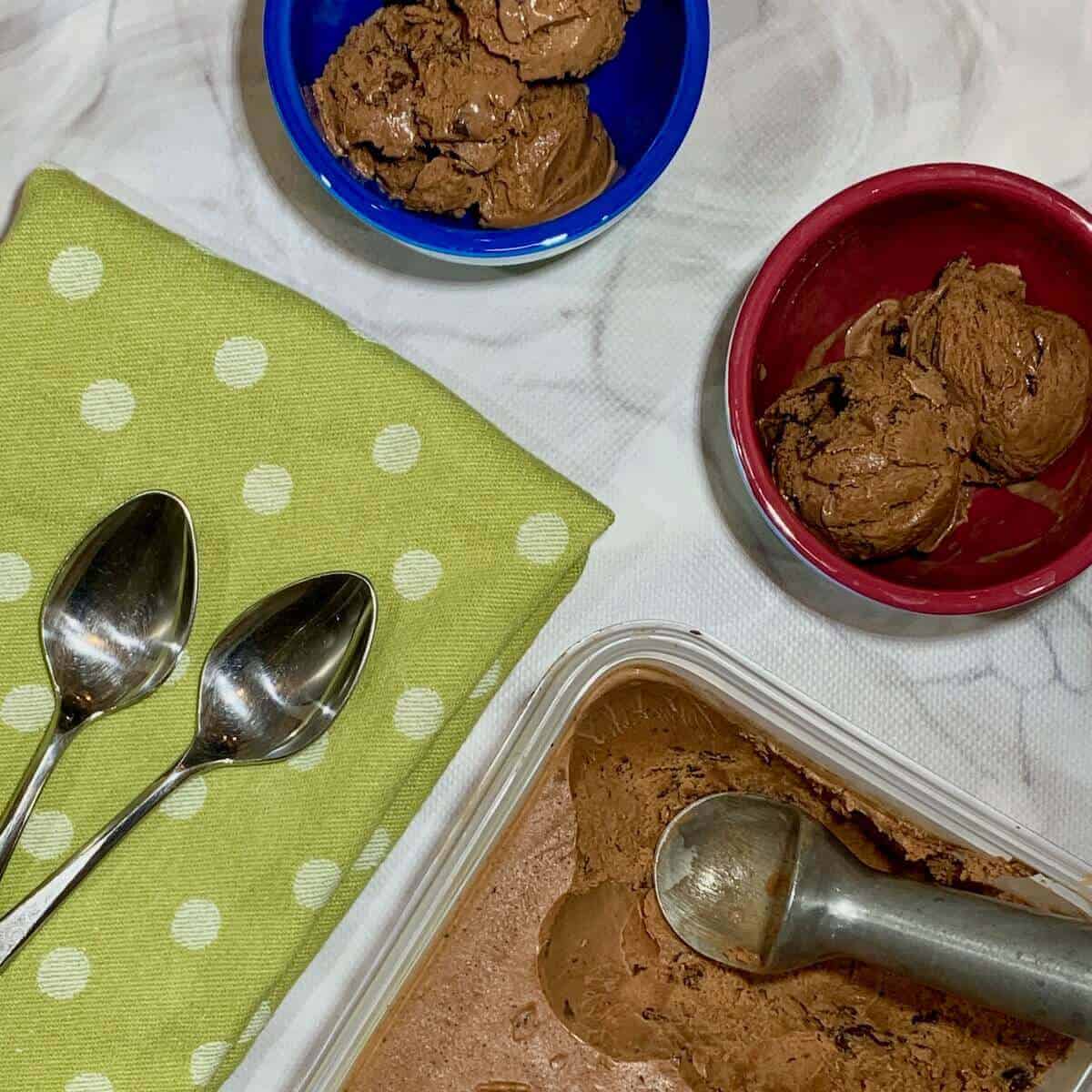 Chocolate Mint Chip gelato in bowls on a green spotted towel next to 2 spoons and gelato tub from overhead.