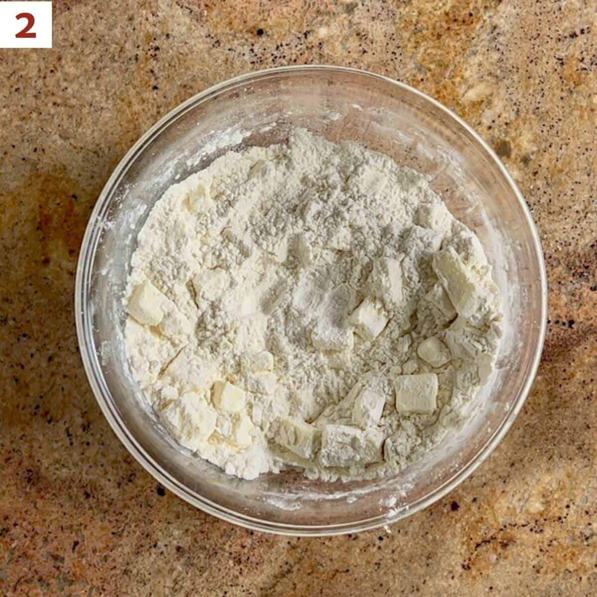 Cubed butter added to the flour mixture in a glass bowl.