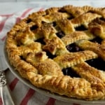 Lattice blueberry pie on a red & white striped towel next to a pie server.