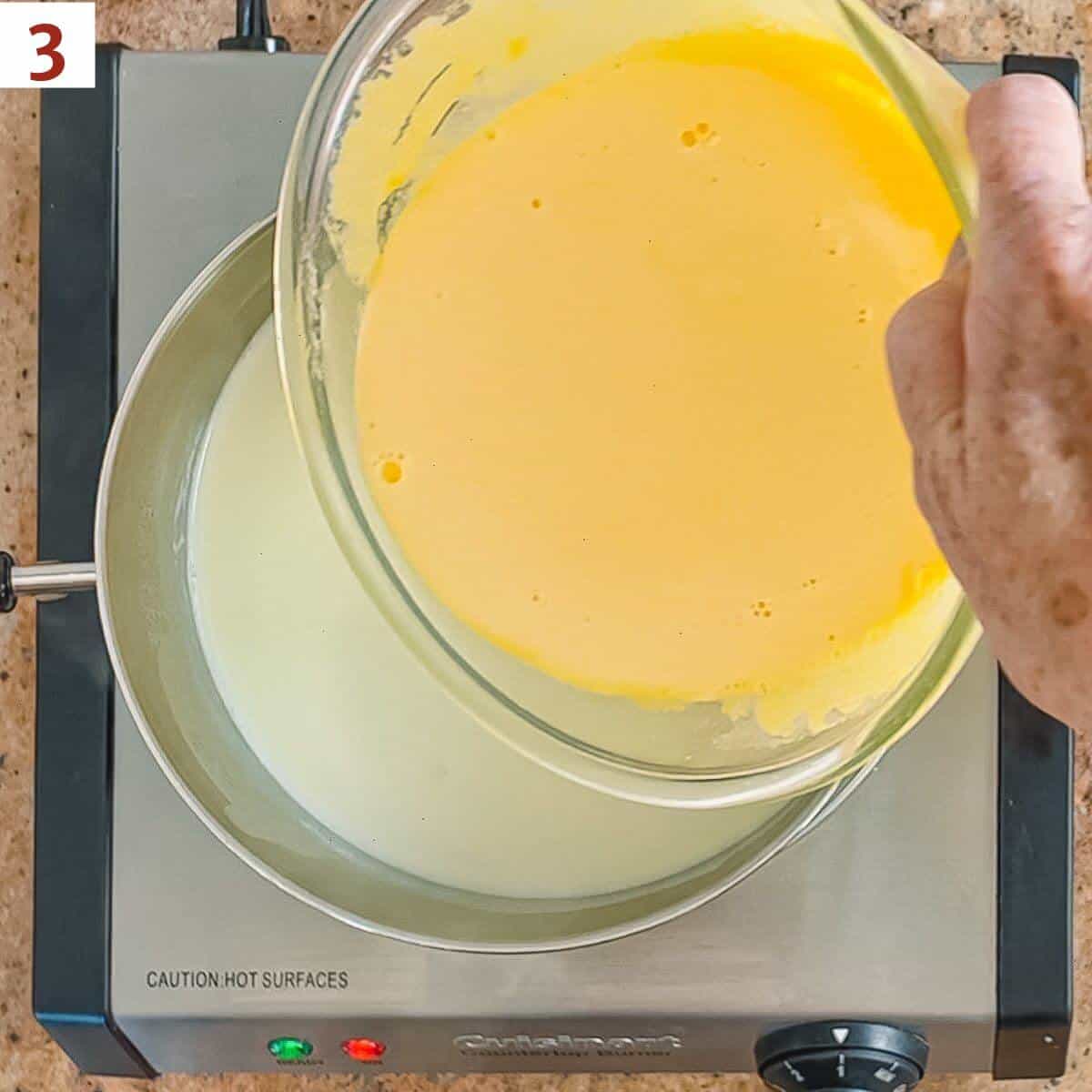 Pouring tempered eggs back into warmed milk in a pan on a hot plate.