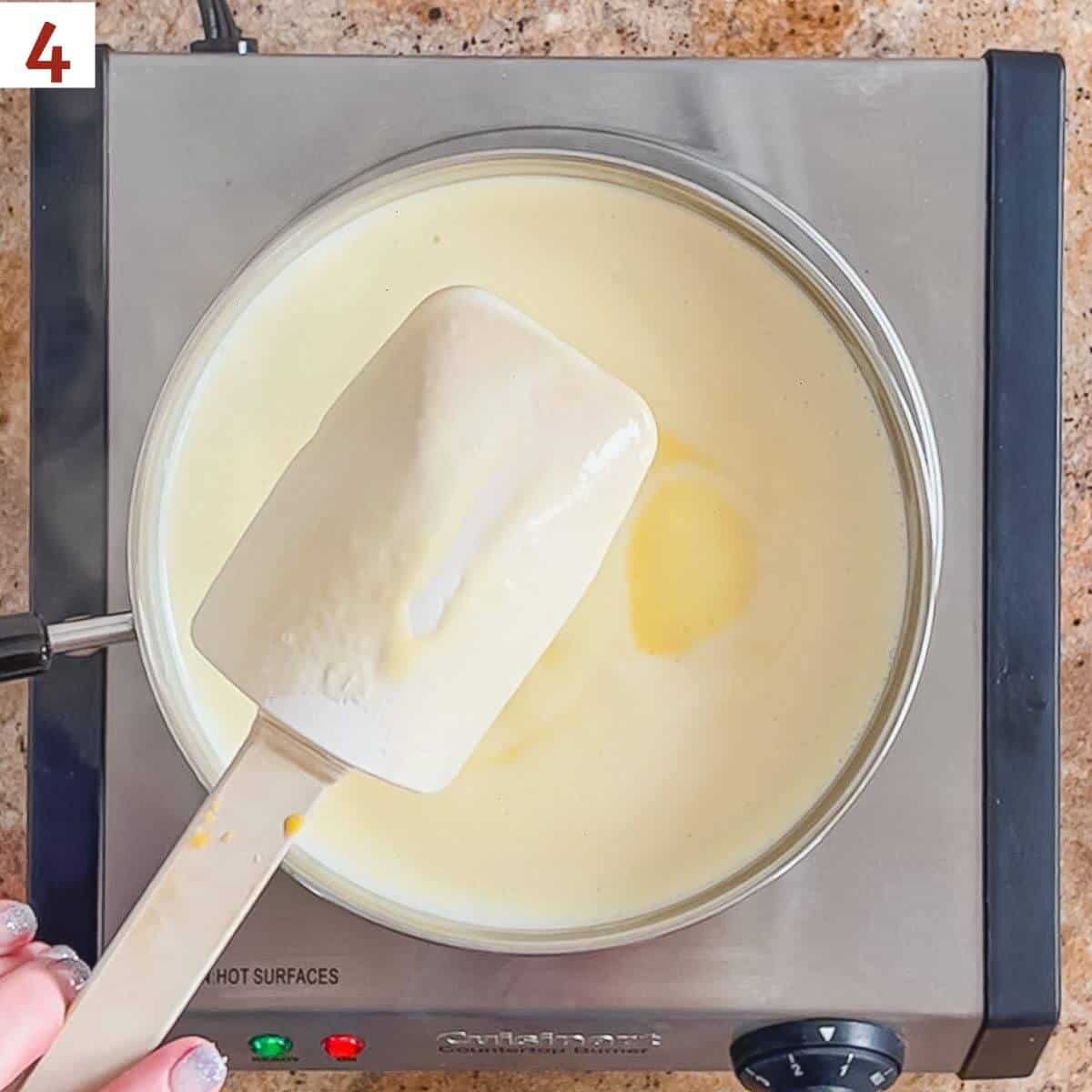 Thickened custard leaving a trail on a spatula over a pan of cooked custard on a hot plate.