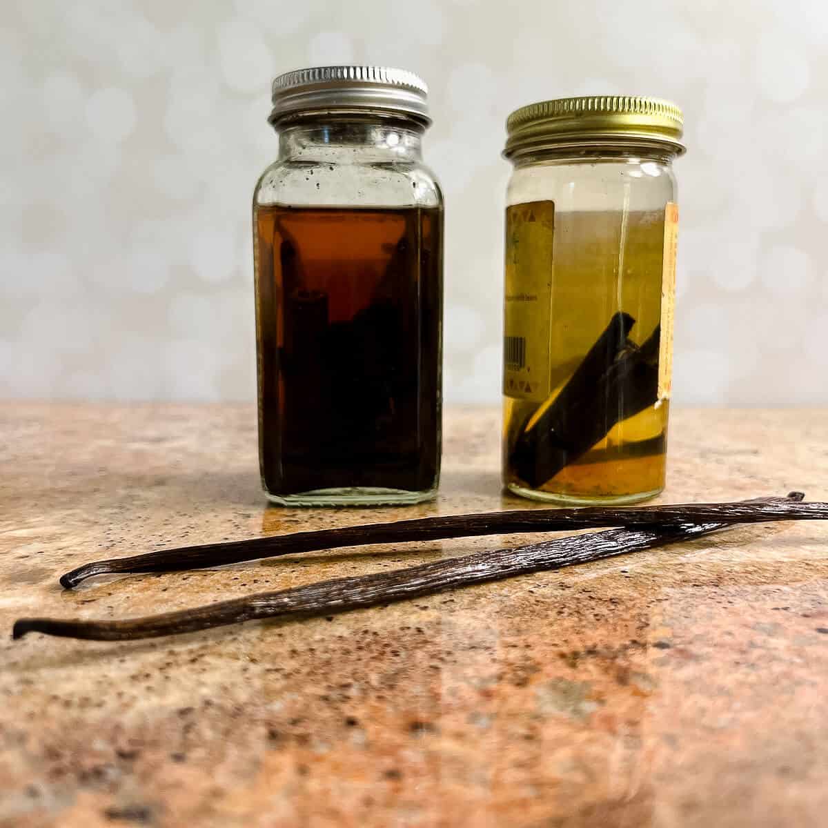 Two jars of homemade vanilla extract behind 2 vanilla beans.