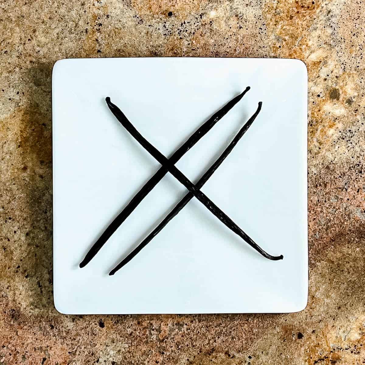 Three Vanilla beans on a square white plate from overhead.