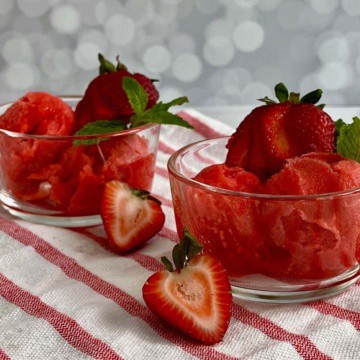 Two bowls of strawberry mint sorbet garnished with strawberries & mint on a red & white striped towel.