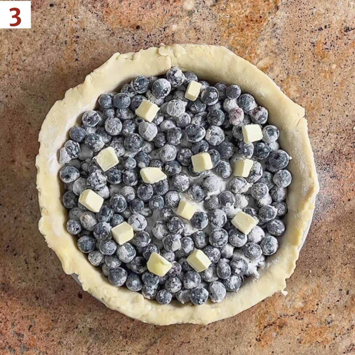 Filled unbaked pie shell with sugared blueberries dotted with butter.