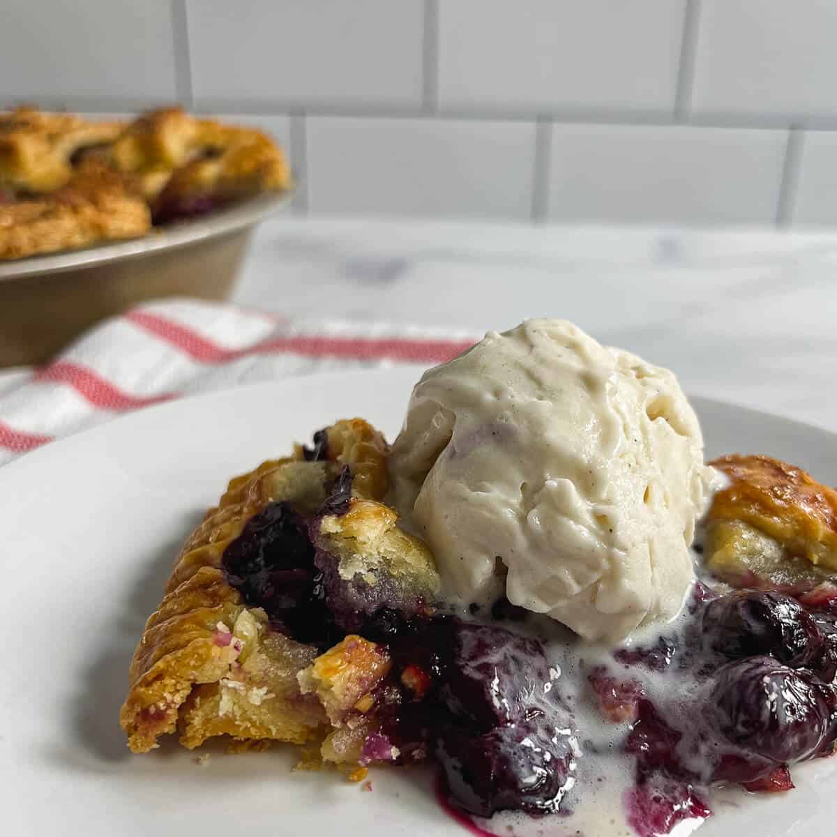 Blueberry pie slice with vanilla ice cream on top on a white plate.