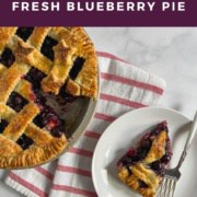 Slice of blueberry pie on a white plate with a fork next to a baked pie with a slice missing on a red & white striped towel from overhead Pinterest banner.