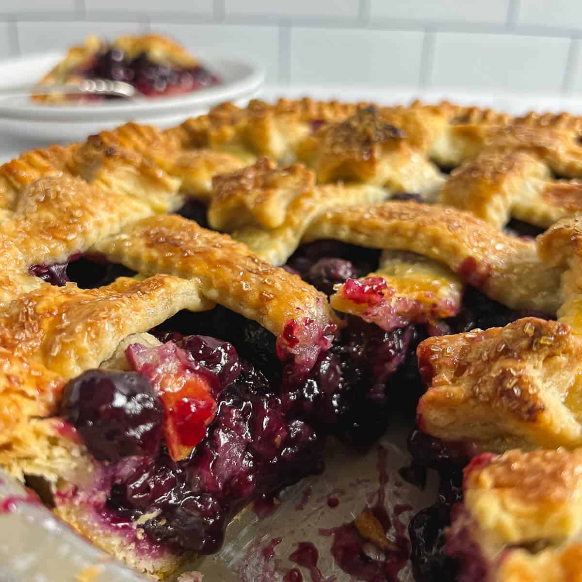 Closeup of cut blueberry pie in the pan with a plated slice behind.