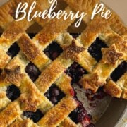 Baked blueberry pie with slice missing next to a pie slicer on a red & white striped towel from overhead Pinterest banner.