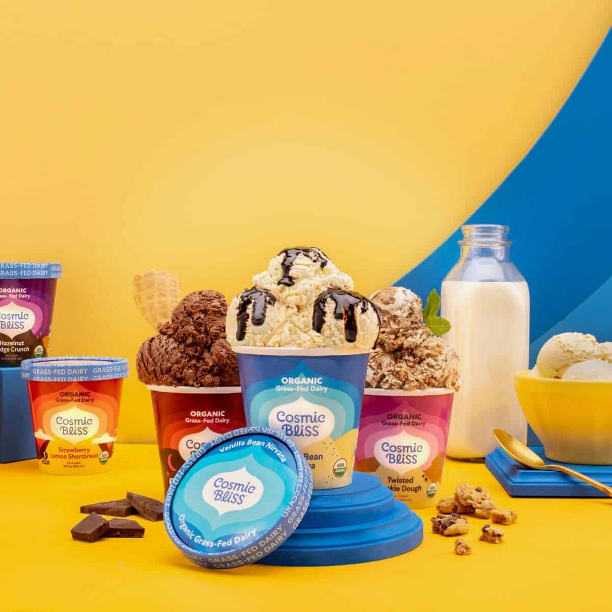 Lineup of Cosmic Bliss ice cream in their tubs with milk on a yellow and blue background.
