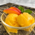 Two scoops of Mango Sorbet in a glass bowl with mango slices.